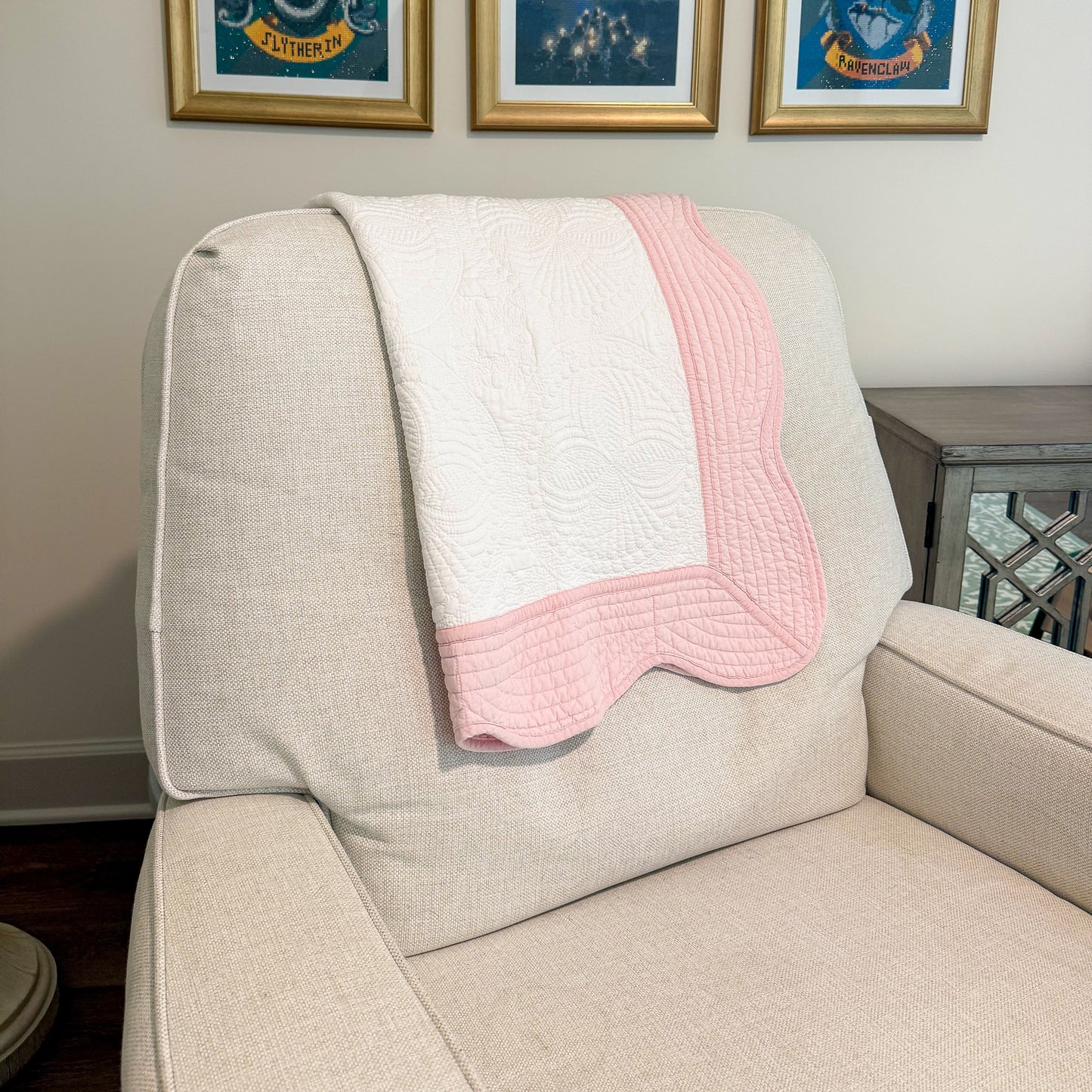 Beige armchair with a pink and white blanket draped over it, framed pictures on the wall.