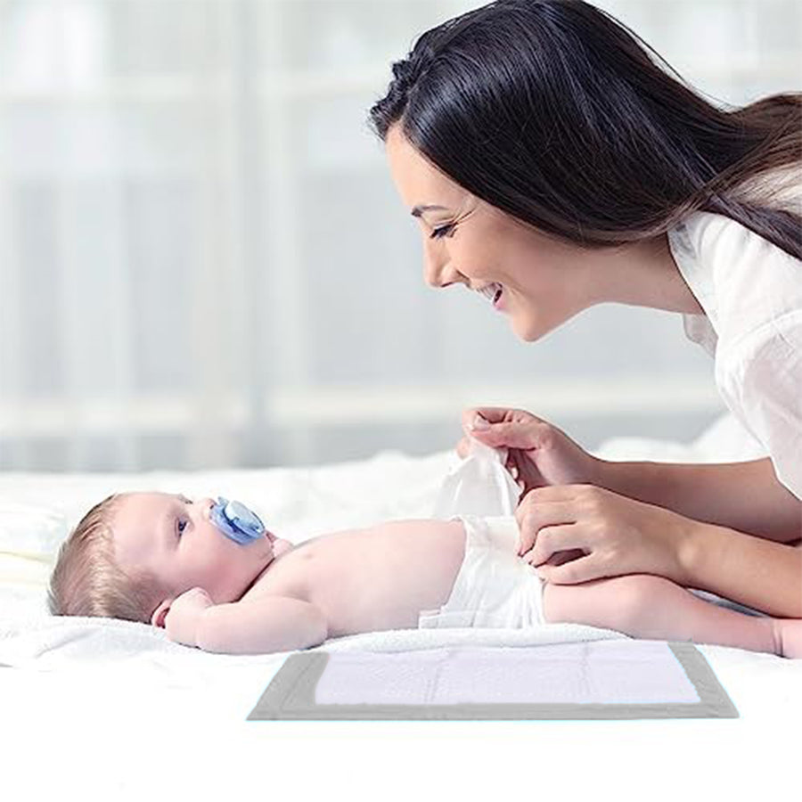 Mom changing a baby's diaper on the disposable changing pad on a bed.