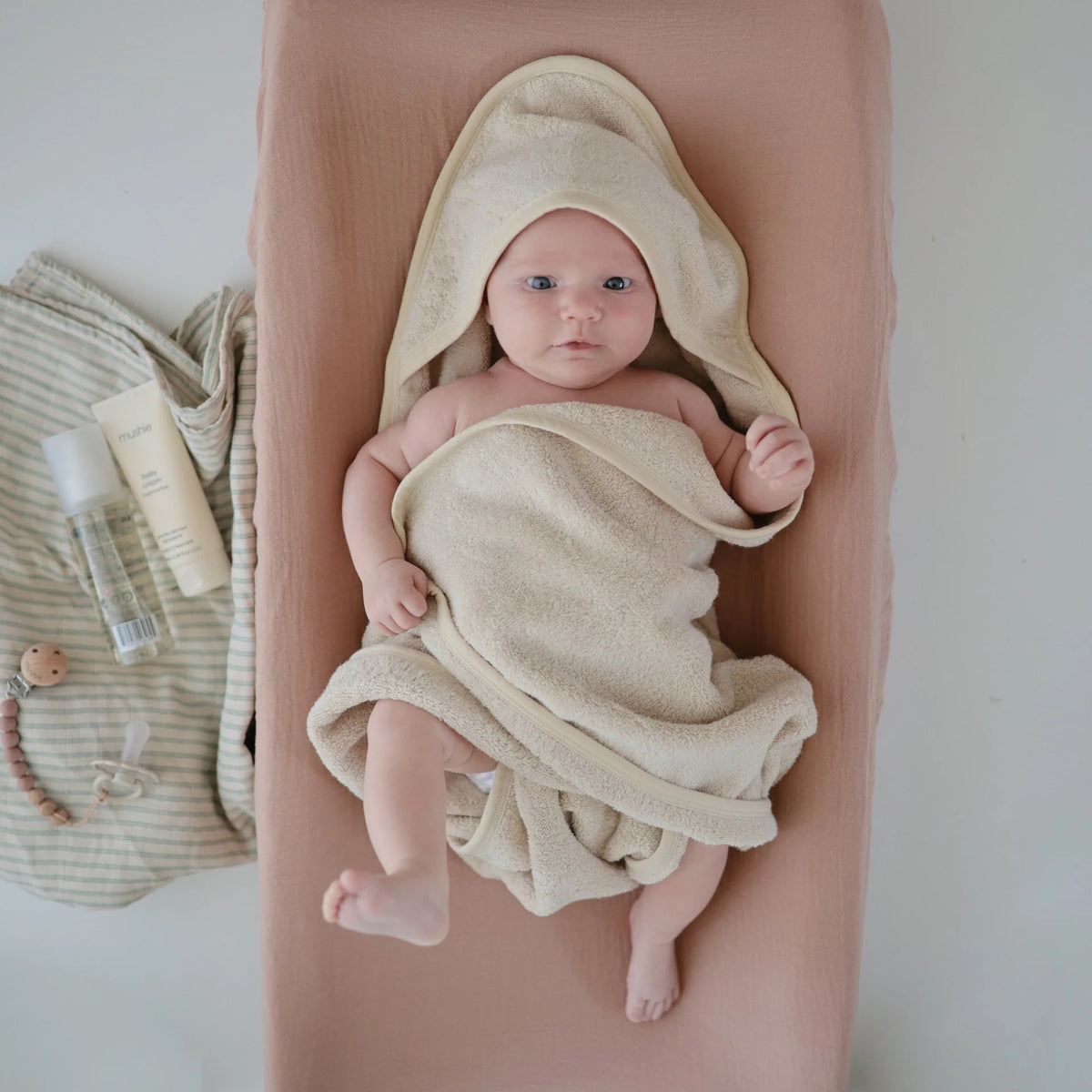 Baby wrapped in the hooded bath towel on a changing pad.