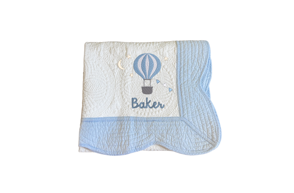 The Heirloom Quilt pictured in the white with blue scallops with Baker and the balloon embroidery in blue.