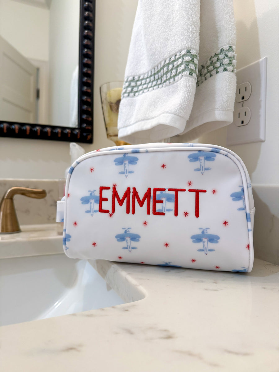 TRVL Stow it Dopp Kit in the David's Airplane print on a bathroom counter with 'Emmett' embroidered in red.