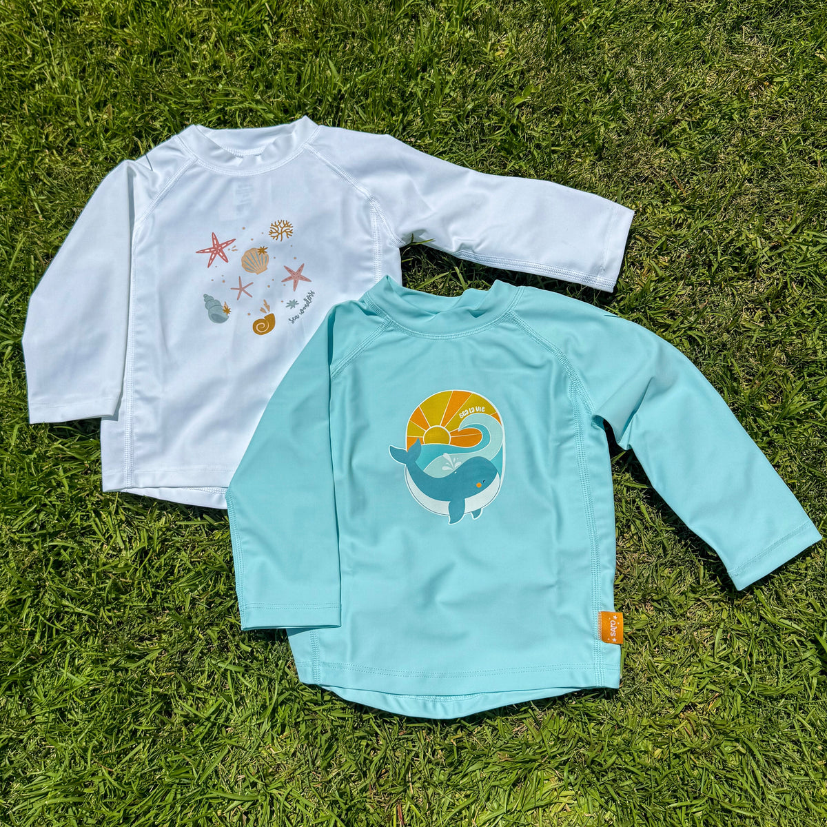 2 swim shirts in a flat lay on grass.