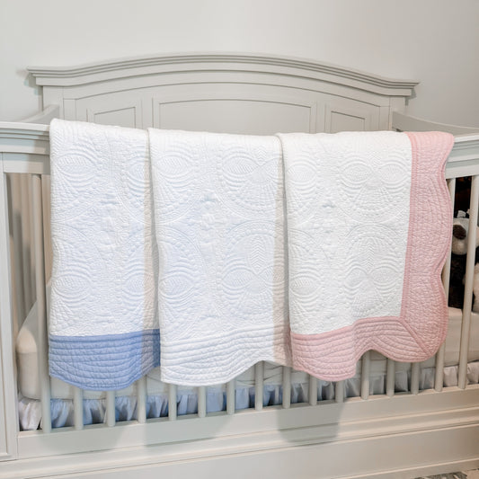 Three baby blankets in blue, white, and pink draped over a crib.