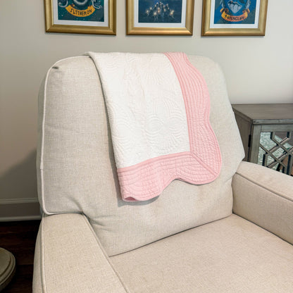 Beige armchair with a pink and white blanket draped over it, framed pictures on the wall.
